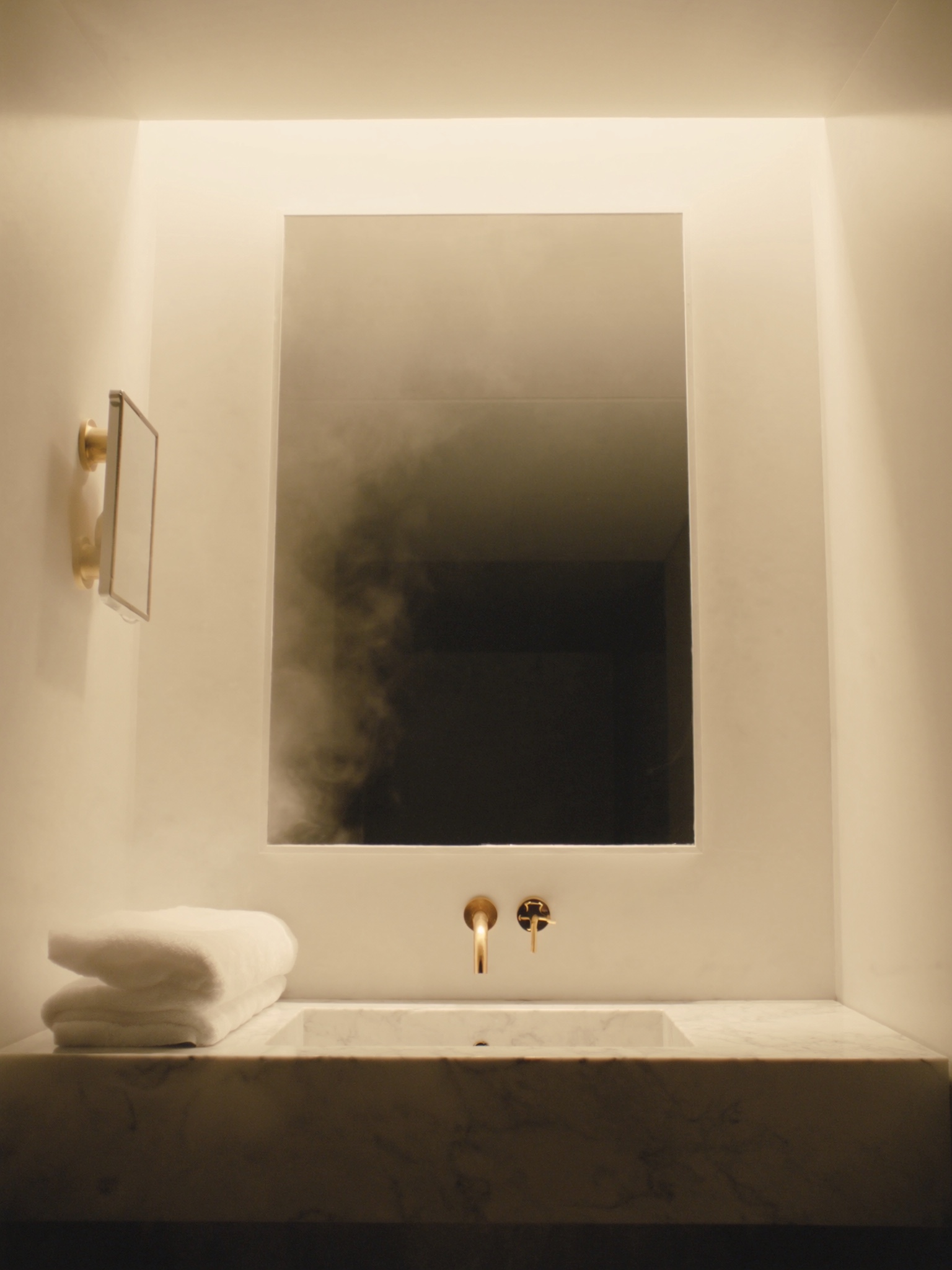 Klarer Spiegel über einem Waschtisch im Hotelbad, warmes Licht